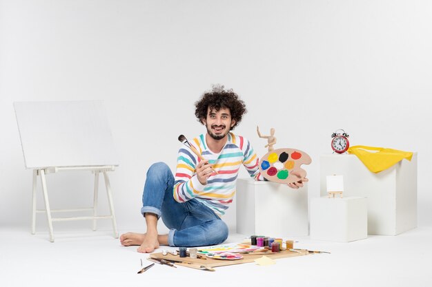 Vista frontal de las pinturas de dibujo de hombres jóvenes en la pared blanca