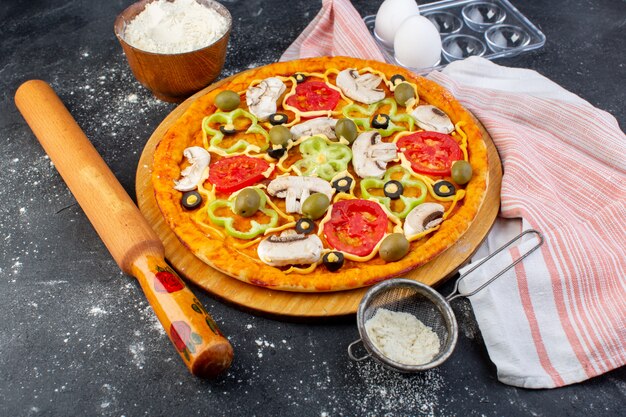 Vista frontal de la pizza de champiñones con tomates rojos pimientos aceitunas todo en rodajas por dentro con aceite y harina en gris