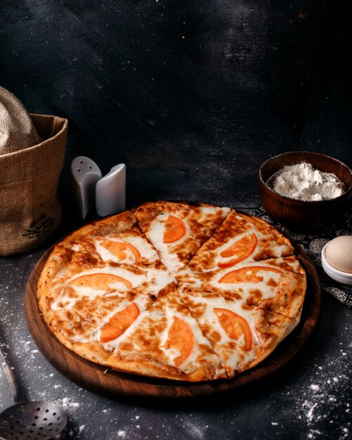 Vista frontal de pizza con queso y tomates rojos sobre la superficie gris