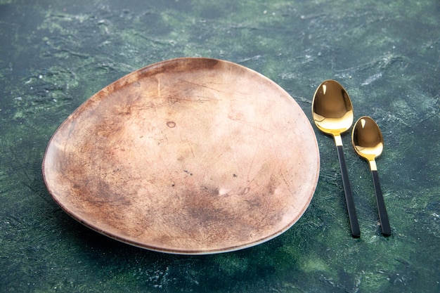 Vista frontal de la placa marrón con cucharas de oro sobre fondo oscuro