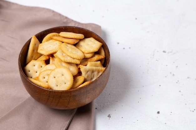 Vista frontal de la placa marrón con sabrosas galletas saladas y patatas fritas en la superficie clara