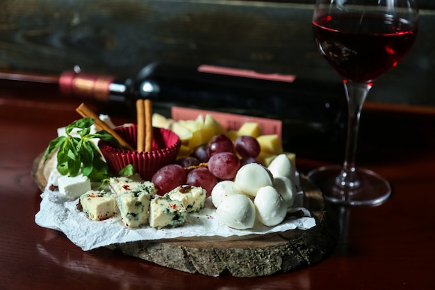 Vista frontal plato de queso mezcla de quesos con uvas y miel con una copa de vino tinto