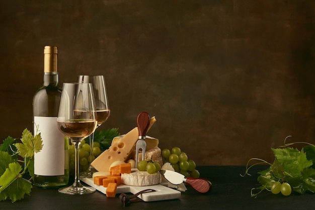 Vista frontal del plato de queso sabroso con uvas y la botella de vino, frutas y copas de vino