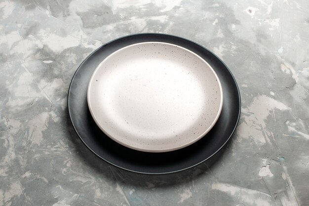 Vista frontal plato vacío redondo de color negro con plato blanco sobre el escritorio gris.
