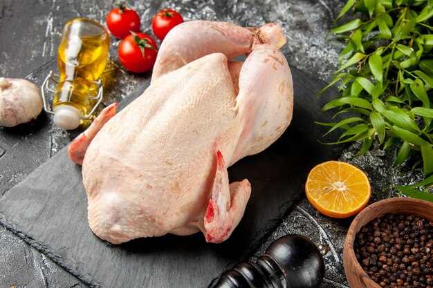 Vista frontal pollo crudo fresco con tomates en la cocina luz-oscura comida animal foto carne de pollo color comida de granja