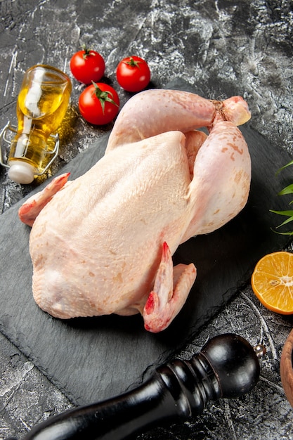 Vista frontal pollo crudo fresco con tomates en la cocina luz-oscura comida animal foto carne de pollo color comida de granja