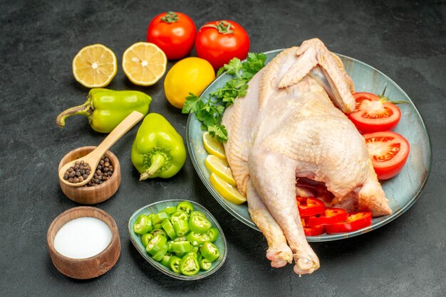 Vista frontal de pollo crudo fresco con tomates, limón y verduras sobre fondo oscuro, ensalada de carne, comida madura, comida.