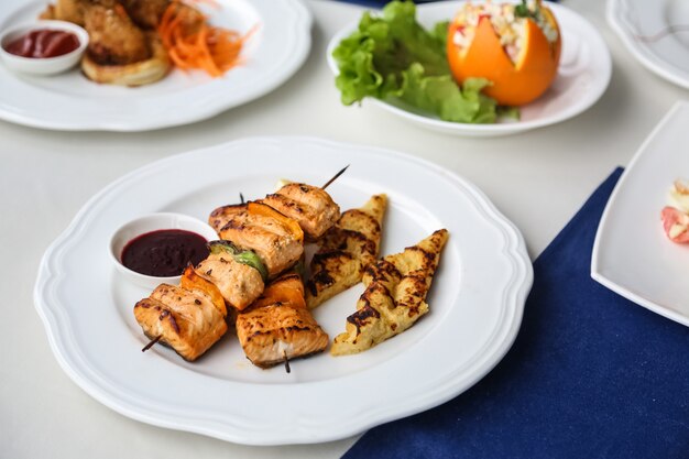 Vista frontal de pollo a la parrilla en brochetas con verduras y puré de papas en un plato con salsa