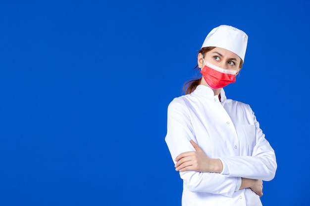 Vista frontal posando a joven enfermera en traje médico con máscara roja sobre azul