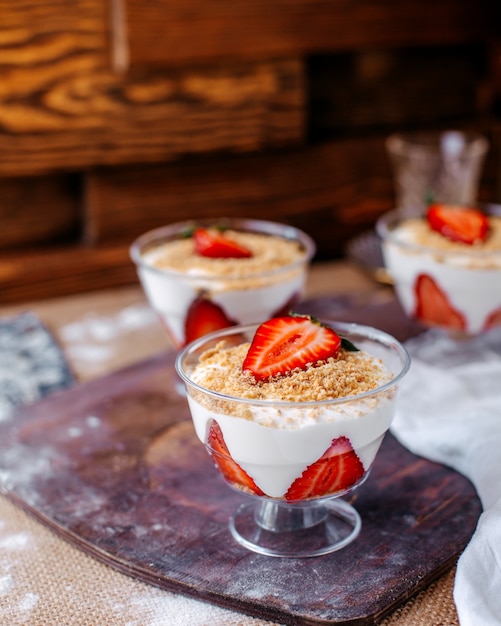 Vista frontal de postre de fresa dentro de pequeños vasos en la superficie marrón