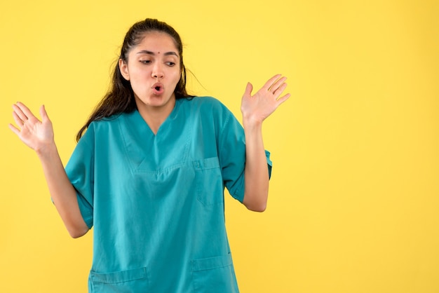 Vista frontal se preguntó bonita doctora abriendo sus manos sobre fondo amarillo