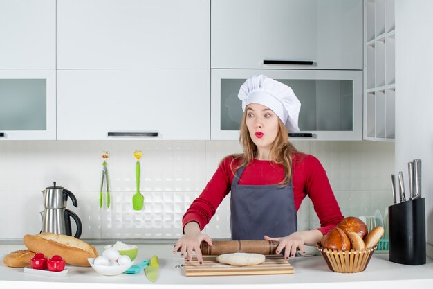 Vista frontal preguntó mujer con sombrero de cocinero y delantal rodando la masa en la cocina