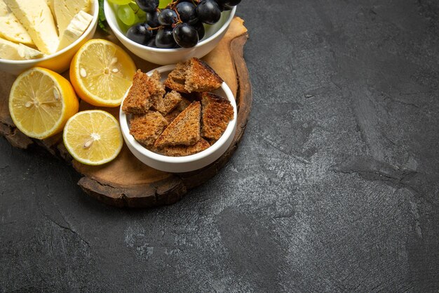 Vista frontal de queso blanco con uvas y rodajas de limón sobre un fondo oscuro comida fruta bollo de leche