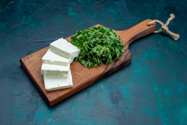 Vista frontal de queso blanco con verduras frescas sobre fondo azul oscuro.