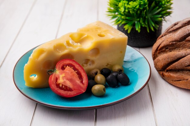 Foto gratuita vista frontal de queso maasdam con tomates y aceitunas en una placa azul sobre un fondo blanco.