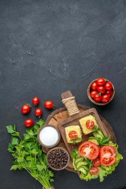 Vista frontal del queso de verduras frescas picadas en la tabla de cortar y el paquete verde de especias sobre superficie negra