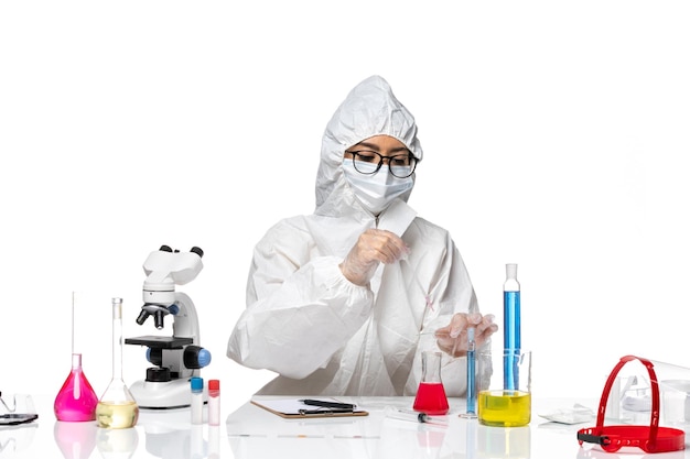 Vista frontal de la química femenina en traje de protección especial que trabaja con soluciones en el laboratorio de química covid de virus de fondo blanco claro