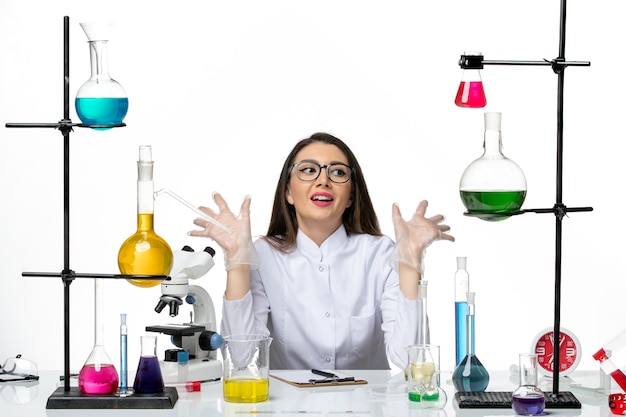 Vista frontal químico femenino en traje médico blanco sentado y posando felizmente sobre fondo blanco ciencia pandemia covid virus de laboratorio