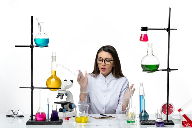 Vista frontal químico femenino en traje médico blanco sentado sobre fondo blanco laboratorio virus covid pandemia ciencia