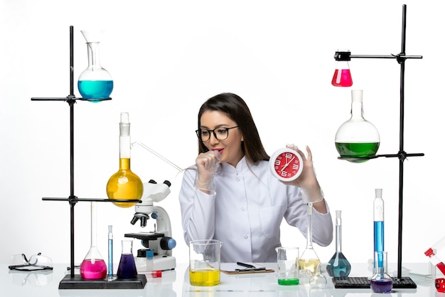 Foto gratuita vista frontal químico femenino en traje médico blanco sosteniendo relojes rojos y tosiendo sobre fondo blanco laboratorio de virus de ciencia covid- pandemia