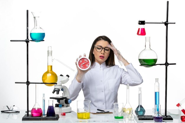 Vista frontal químico femenino en traje médico blanco sosteniendo relojes sobre fondo blanco claro laboratorio de virus de ciencia covid- pandemia