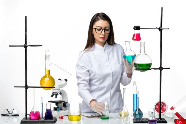 Vista frontal químico femenino en traje médico estéril sosteniendo frascos con soluciones sobre fondo blanco virus covid-ciencia pandémica