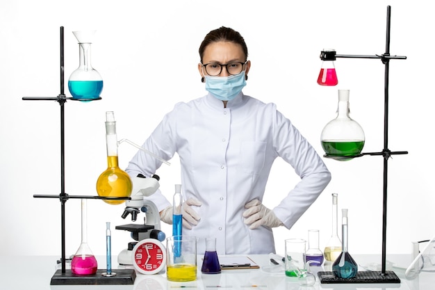 Vista frontal químico femenino en traje médico con máscara posando sobre fondo blanco laboratorio de química de virus covid- splash