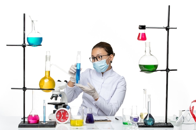 Vista frontal químico femenino en traje médico con máscara con solución azul sobre fondo blanco laboratorio de química de virus splash covid