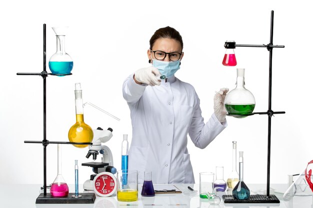 Vista frontal químico femenino en traje médico con máscara sosteniendo inyección sobre fondo blanco laboratorio de química de virus covid splash