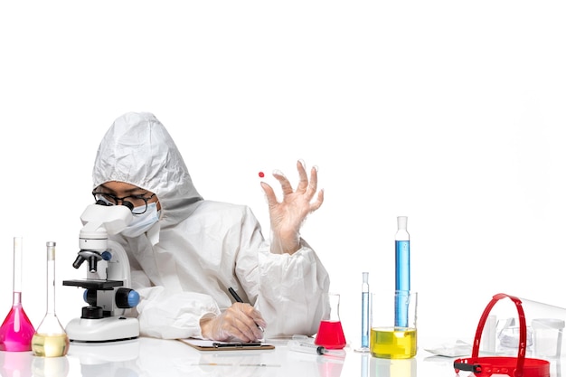 Vista frontal químico femenino en traje de protección especial comprobando la muestra en la química del virus de escritorio blanco salud de la pandemia de covid