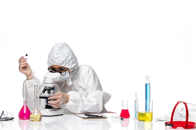 Vista frontal químico femenino en traje de protección especial comprobando muestras en la química del virus de escritorio blanco covid- salud pandémica