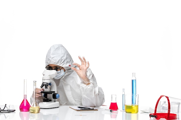 Vista frontal químico femenino en traje de protección especial comprobando muestras sobre fondo blanco química del virus covid-salud pandémica