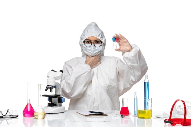 Vista frontal químico femenino en traje de protección especial sosteniendo frascos vacíos en el escritorio blanco salud virus química covid