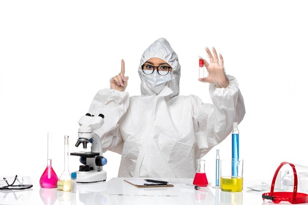 Vista frontal químico femenino en traje de protección especial sosteniendo el matraz sobre fondo blanco claro virus salud química covid-