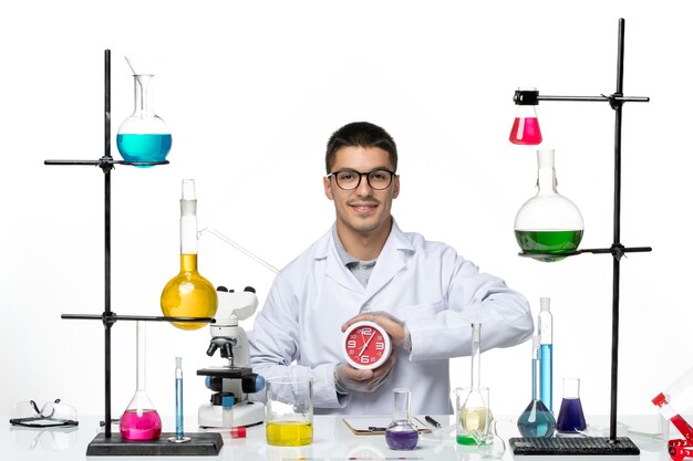 Vista frontal químico masculino en traje médico blanco sosteniendo relojes rojos sobre fondo blanco laboratorio de ciencias de la enfermedad del virus covid