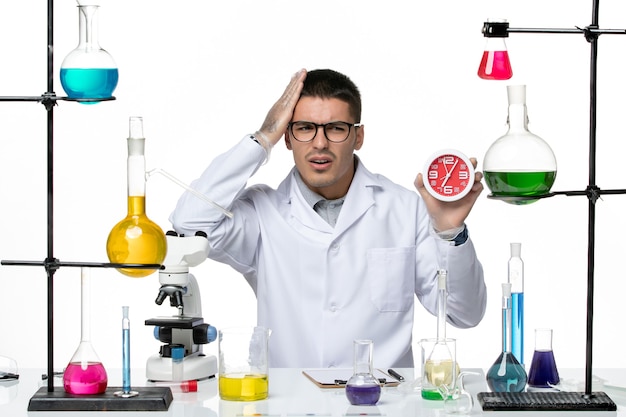Vista frontal químico masculino en traje médico blanco sosteniendo relojes sobre fondo blanco laboratorio de ciencias de la enfermedad del virus covid
