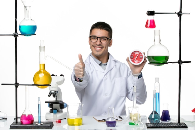 Vista frontal químico masculino en traje médico blanco sosteniendo relojes sonriendo sobre fondo blanco laboratorio de ciencias de la enfermedad del virus covid