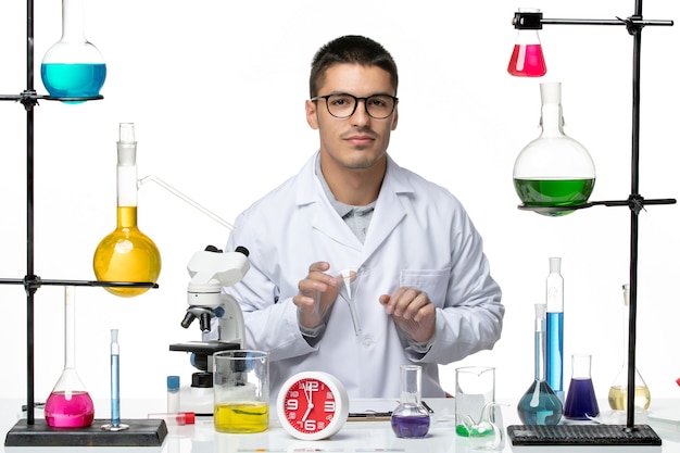Vista frontal químico masculino en traje médico blanco trabajando con soluciones sobre fondo blanco ciencia covid-laboratorio virus pandémico