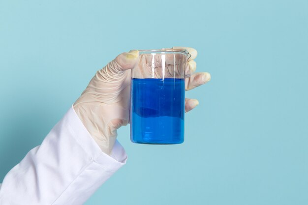 Vista frontal del químico sosteniendo el matraz con solución en la superficie azul