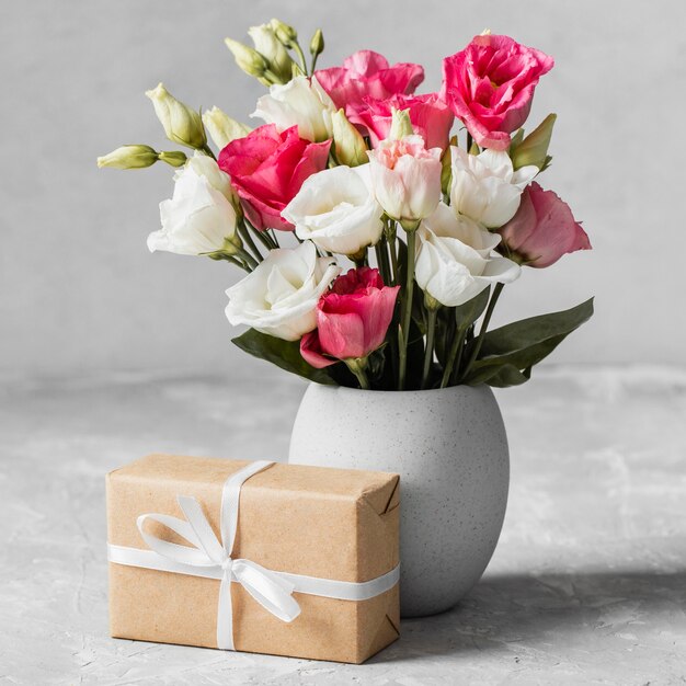 Vista frontal ramo de rosas en un jarrón junto a un regalo envuelto