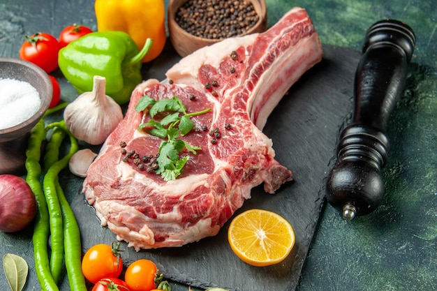Vista frontal de la rebanada de carne cruda con verduras frescas y pimienta sobre una superficie azul oscuro
