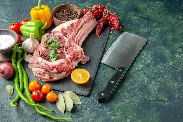 Vista frontal de la rebanada de carne cruda con verduras frescas, sal y pimienta sobre una superficie azul oscuro