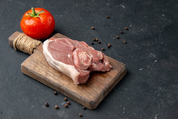 Vista frontal rebanada de carne fresca carne cruda con tomate sobre fondo oscuro plato de barbacoa pimienta comida de cocina ensalada de comida de vaca comida de animal
