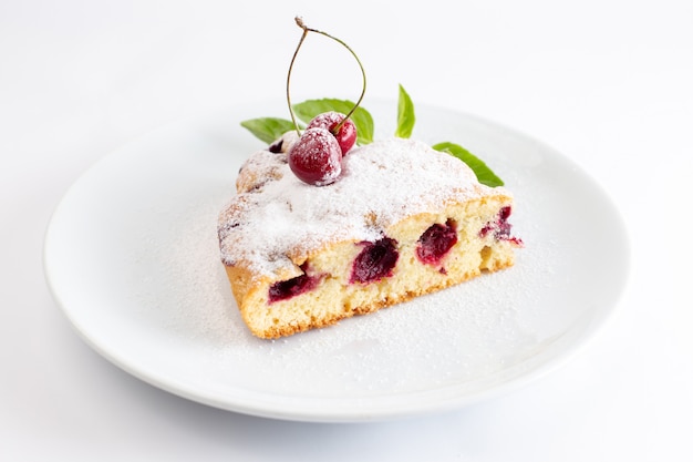 Vista frontal de la rebanada de pastel de cereza deliciosa y deliciosa dentro de un plato blanco sobre la superficie blanca