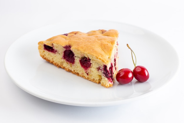 Vista frontal de la rebanada de pastel de cereza dentro de un plato blanco sobre la superficie blanca