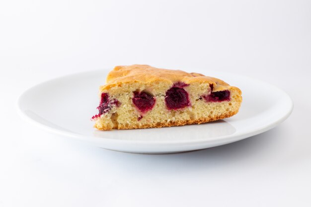 Vista frontal de la rebanada de pastel de cereza dentro de un plato blanco sobre la superficie blanca