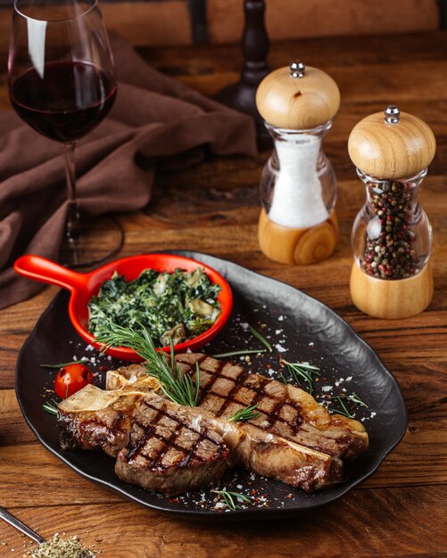 Una vista frontal de las rebanadas de carne frita con verduras dentro de la placa negra con una copa de vino en el escritorio de madera marrón comida comida carnes