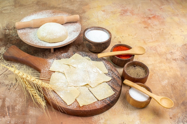 Vista frontal de las rebanadas de masa cruda con harina y condimentos en el plato de comida de escritorio crema pasta