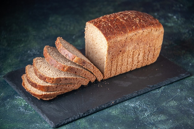 Vista frontal de las rebanadas de pan negro en la pizarra sobre fondo angustiado de colores mezclados