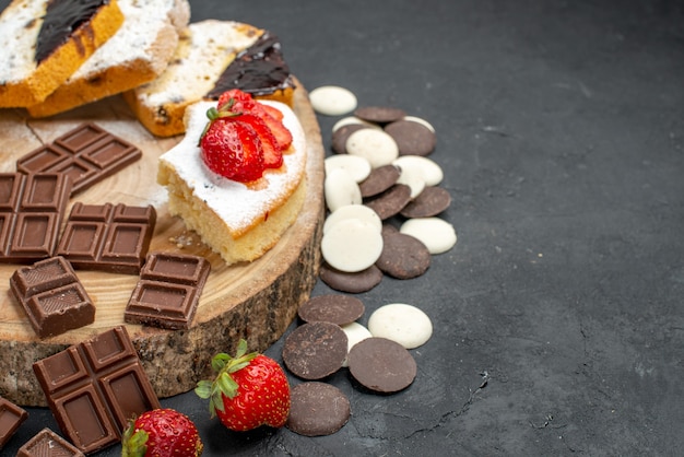 Vista frontal de las rebanadas de pastel con galletas y barras de chocolate sobre fondo oscuro